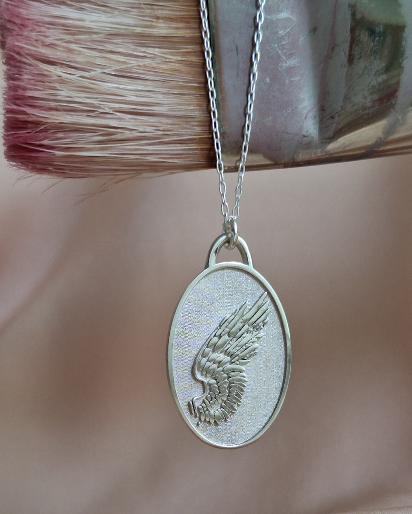 Silver pendant with angel wings design on a chain, close-up.